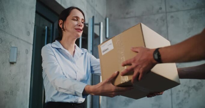 Postal Service Worker Bringing Parcel Box for Client Working in Modern Office. Businesswoman Taking Package with Online Shopping Order, Signing POD on Smartphone. Delivery Service. Slow Motion.