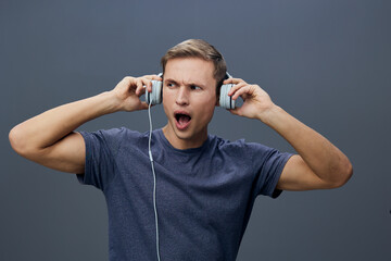 Frustrated young man wearing casual t-shirt, upset expression, holding large headphones, isolated...