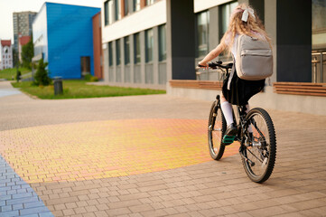 girl riding bicycle to school with backpack on urban campus, morning routine. young student...