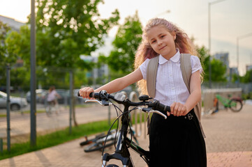 young girl with bicycle wearing backpack in urban park setting. casual outdoor exploration and...