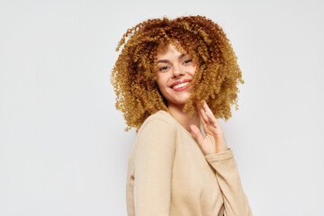 Smiling woman with curly hair posing against a light gray background, cheerful expression conveys...