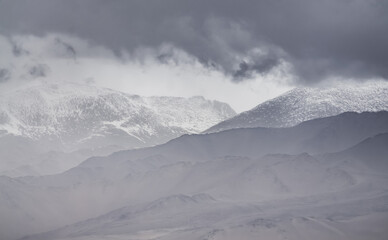 Panorama of mountain peaks with snow and glaciers, a landscape in the highlands of the Tien Shan in Pamir in cloudy weather with clouds and rain, high-mountain steppe and mountains in the background