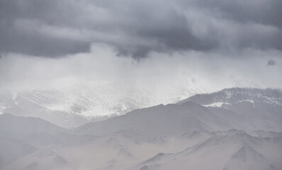 Panorama of mountain peaks with snow and glaciers, a landscape in the highlands of the Tien Shan in Pamir in cloudy weather with clouds and rain, high-mountain steppe and mountains in the background