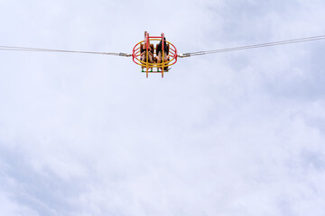 A moment on a catapult ride at an amusement park, where two young women sit upside down in a spherical cage against the sky. A thrilling ride for adults and teenagers.