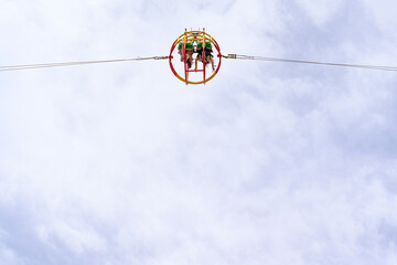 A moment on a catapult ride at an amusement park where two young women sit upside down in a spherical cage against the sky with their arms raised in delight, their hair flying. 