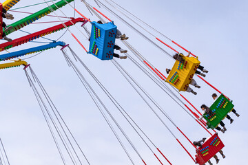 A large colorful carousel in action, on which people of different ages ride, in an amusement park against the background of the blue sky, close-up, rear view.