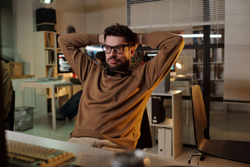 Caucasian man leaning back with hands behind head wearing headset in office with computer monitors...