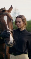 Fototapeta premium An elegant woman strokes a horse's muzzle and poses looking at the camera