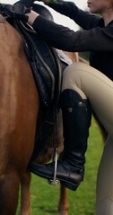 An elegant woman sits in the saddle on a horse and smiles looking at the camera