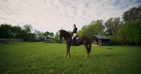 A focused woman trains to ride a horse on a farm on a summer day