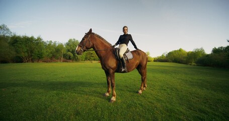 A stylish woman poses sitting on a horse on a cloudy day at a farm