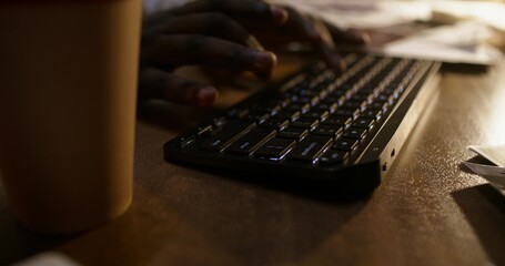 A businessman uses a computer while sitting at his desk in a dark office. Close-up of his hands,...