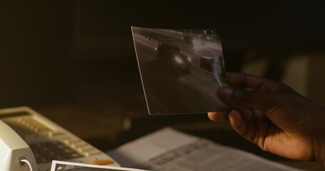 The detective examines the photographs. Close-up of his hands, unrecognizable persona