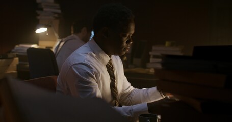 Two serious-looking men are working in a gloomy office. They're sitting at their desks.