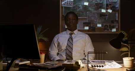 Portrait of a detective in an office. He looks at the camera while sitting at the table. Evidence...