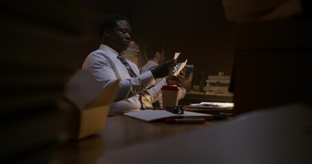 The two detectives work together. They study crime scene photos and talk while sitting at their desks.