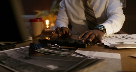 The detective uses a computer while sitting at his desk in the office. Close-up of his hands on the keyboard