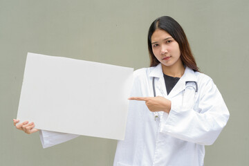 Young woman doctor wearing white lab coat and stethoscope holding empty placard with copy space