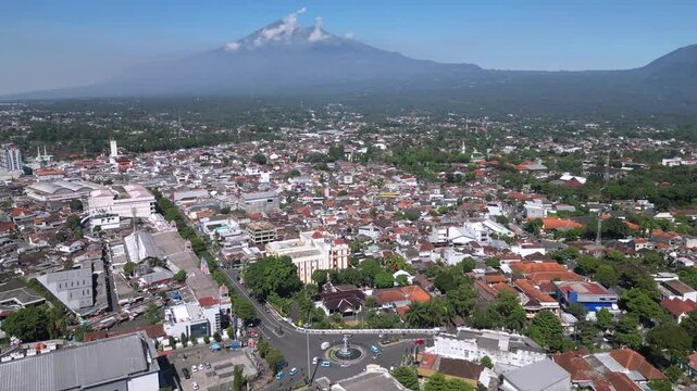 A cityscape of Salatiga with urban buildings in the foreground, framed by the majestic Mount Merbabu rising peacefully in the background under a clear sky.