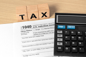Tax calculation concept with IRS 1040 form, calculator, and wooden blocks spelling TAX. U.S. income...
