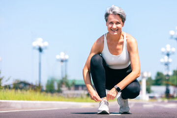 Smiling Active Woman Tying Shoelaces Before Outdoor Workout on a Sunny Day in the City