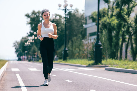 Confident Mature Woman Jogging Outdoors on a Sunny Day in Sportswear and Smartwatch