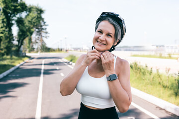 Confident woman fastening helmet before bike ride on a sunny summer day in city park lane
