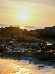 Orange sunlight reflects off the calm ocean as the sun sets over the horizon, painting the sky with beautiful clouds