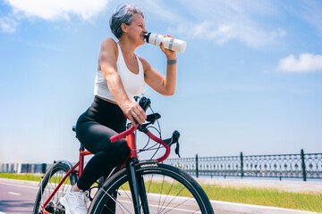 Senior Woman Drinking Water While Riding Bicycle Along Seafront on Sunny Summer Day