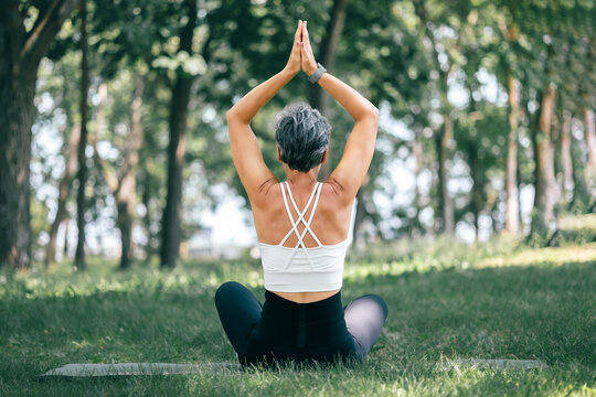 Mature Woman in Sukhasana with Urdhva Namaskarasana Pose Outdoors in Tranquil Forest Setting