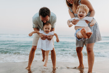 A young family with two toddler children having fun on beach on summer holiday.