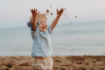 Toddler boy playing with sand on beach during summer holiday, having fun.