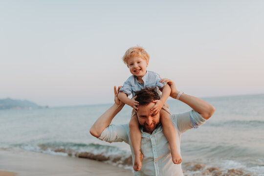 Father carrying toddler on the shouolderes, walking on beach on summer holiday.