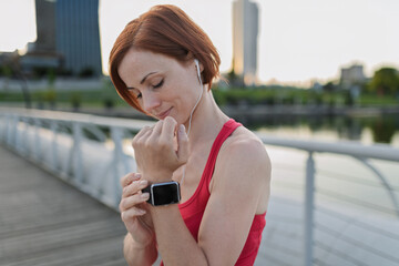 Runner checking her performance on a smartwatch during her morning run across a city bridge.