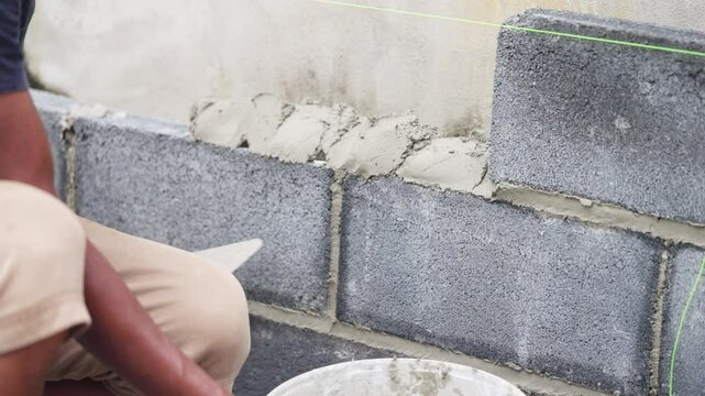 A man is laying bricks and using a trowel to spread mortar. He is wearing a white shirt