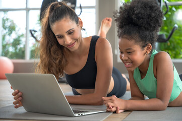 Sportive fitness mother and daughter looking at laptop after doing exercise in house gym, family...