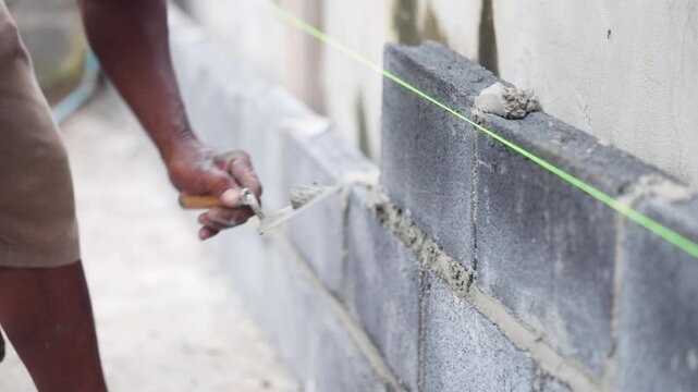 A man is laying a brick wall. He is using a green laser line to mark the wall