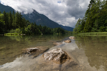 Fels im Wasser im Vordergrund Berg mit bewölkten Himmel am Hintersee in den Alpen bei Berchtesgarden in Deutschland