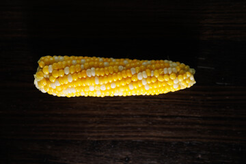 A deliciously boiled corn on the cob served in a restaurant style on a dark background. The vibrant yellow corn is presented with melted butter and fresh herbs, creating an inviting contrast and a coz