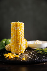 A deliciously boiled corn on the cob served in a restaurant style on a dark background. The vibrant...
