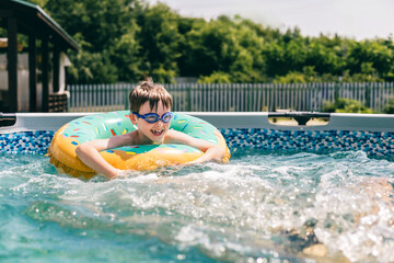 Happy boy floating in colorful donut ring with goggles in outdoor backyard pool on sunny day