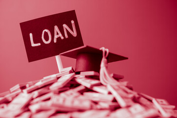 Mortarboard on heap US dollar banknotes and LOAN label monochrome tone. Student loan or debt,...
