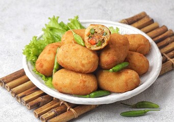 Kroket kentang. Croquettes are lumps of finely mashed potatoes filled with seasoned minced meat and mixed with vegetables such as carrots or green beans. The croquettes are coated with beaten egg and 