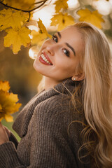Stylish young blonde woman in autumn park walks with yellow leaves collects yellow bouquet. Autumn...