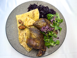 Two roast duck legs with potato pancake, red cabbage and fresh salad. Traditional dish served at duck feast. Tasty Slovak or Hungarian cuisine, top view on plate.