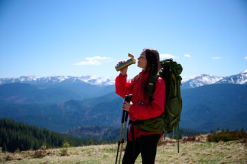 Woman in hiking gear taking a sip of water during mountain hike. Sporty female standing in front of...