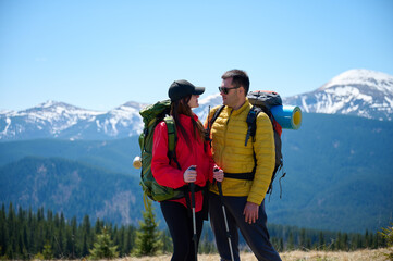 Two hikers taking a break on a mountain ridge. Sporty couple with hiking backpacks standing on...