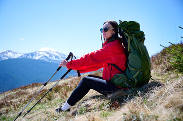 Female hiker with backpack and trekking poles walking in the mountains. Adventure lifestyle in...
