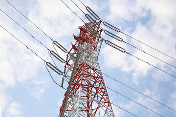 Red and white high-voltage transmission tower in Japan against a cloudy sky.