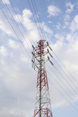 Red and white high-voltage transmission tower in Japan against a cloudy sky.